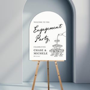 K&ouml;nnte beinhalten: Ein wei&szlig;es Schild mit schwarzem Text und einer Zeichnung von Sektgl&auml;sern. Der Text lautet "Willkommen zur Verlobungsfeier Zur Feier von Chase & Michele 09.18.25"