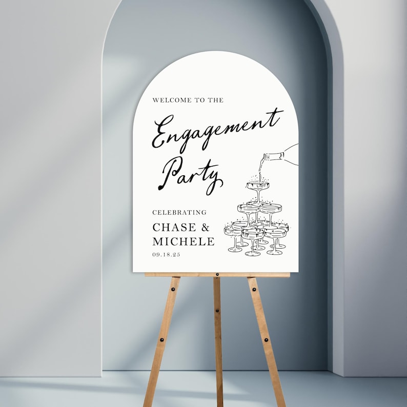 K&ouml;nnte beinhalten: Ein wei&szlig;es Schild mit schwarzem Text und einer Zeichnung von Sektgl&auml;sern. Der Text lautet "Willkommen zur Verlobungsfeier Zur Feier von Chase & Michele 09.18.25"