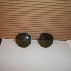 May include: A pair of round, silver-rimmed sunglasses with dark lenses. The sunglasses are on a white surface.