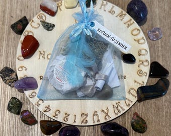 May include: A wooden Ouija board with a blue drawstring bag containing various items, surrounded by a variety of colorful stones. The board has letters, numbers, and the words "Return to Sender" printed on it.