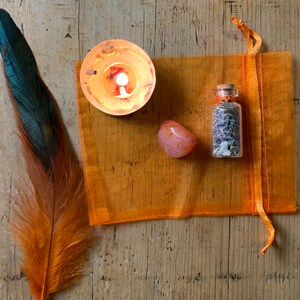 May include: A small orange mesh bag with a clear glass bottle filled with dried lavender, a small orange carnelian stone, and a small orange candle.
