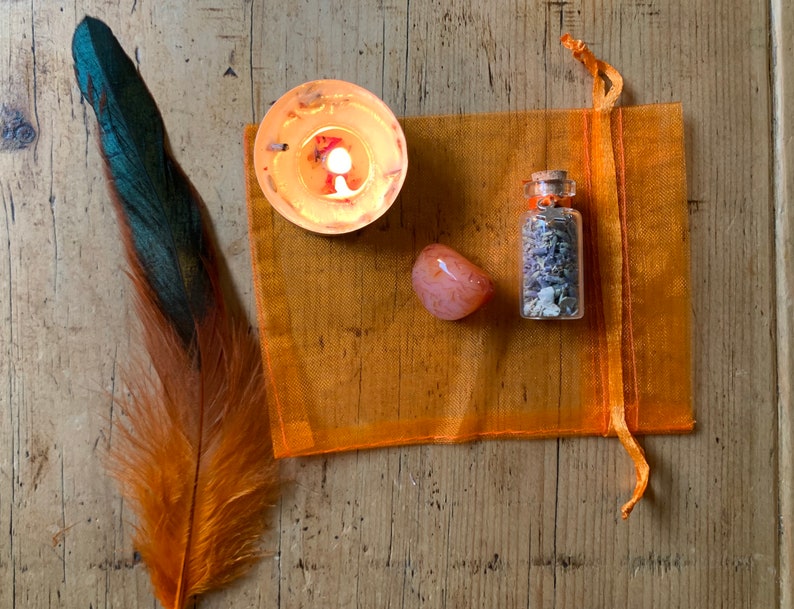 May include: A small orange mesh bag with a clear glass bottle filled with dried lavender, a small orange carnelian stone, and a small orange candle.