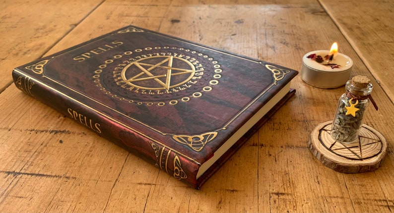 Peut inclure: Un journal reli&eacute; en cuir marron avec des accents dor&eacute;s et le mot "Spells" en relief sur la couverture. Le journal est ouvert pour r&eacute;v&eacute;ler un pentagramme avec un cercle dor&eacute; autour. Une petite bouteille en verre avec un charme d'&eacute;toile dor&eacute;e est pos&eacute;e sur un sous-verre en bois avec un motif de pentagramme. Une petite bougie avec une flamme est pos&eacute;e sur un sous-verre argent&eacute;.