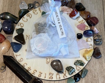 May include: A wooden Ouija board with a white cloth bag labeled "Health & Healing" and a variety of colorful stones surrounding it.