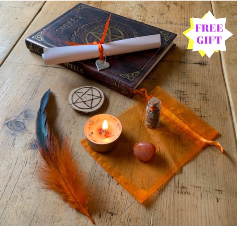 May include: A witchy spell kit with a brown leather-bound book with the word "Spells" on the cover, a white scroll tied with an orange ribbon, a small orange feather, a wooden pentagram, a small orange candle, a small orange pouch with a glass vial of herbs, and a red stone.