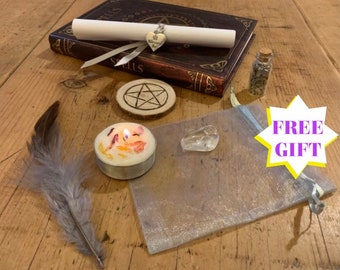 May include: A witchy spell kit with a book, a candle, a feather, a crystal, a small bottle, a wooden pentagram, and a scroll. The kit is on a wooden table. The scroll has a charm attached to it that says "Blessed Be".
