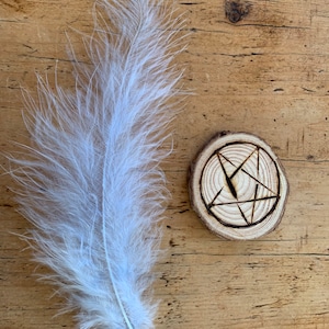 May include: A white feather and a wooden circle with a carved pentagram design.