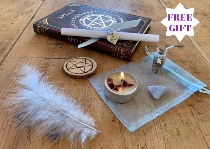 May include: A witchy spell kit with a brown leather-bound book with the word "Spells" on the cover, a white feather, a small wooden circle with a pentagram carved into it, a small glass bottle with a silver star charm, a tealight candle with red wax, a small blue stone, and a blue organza bag.
