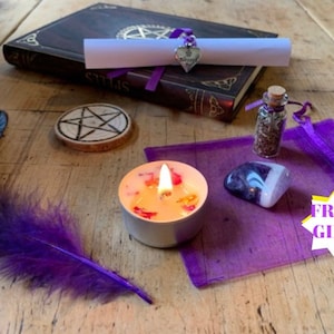 Pode incluir: Uma pena preta e roxa, uma pequena vela branca com detalhes laranja e vermelho, uma bolsa roxa com um pequeno cristal de ametista, uma pequena garrafa de vidro com rolha de cortiça cheia de ervas, um círculo de madeira com um desenho de pentagrama, um livro fechado com uma fita roxa e um pedaço de papel enrolado com um amuleto prateado, e uma estrela amarela com o texto "PRESENTE GRÁTIS" em uma mesa de madeira.