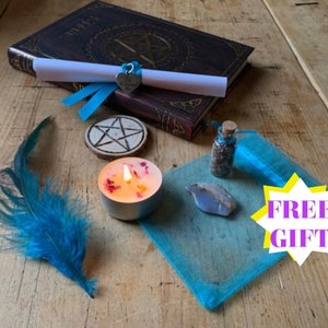 May include: An assortment of mystical items on a wooden surface. Includes a leather-bound book, a scroll tied with blue ribbon, a wooden pentagram, a lit candle with flower petals, a small bottle, a blue crystal, a blue feather, and a blue mesh bag.