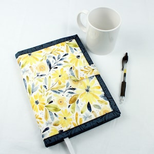 May include: A blue and white floral notebook cover with a yellow floral pattern. The cover has a flap that closes with a velcro closure.