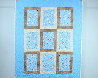 May include: A blue baby quilt with a white border and a patchwork design featuring brown and white squares with a pattern of small dogs.