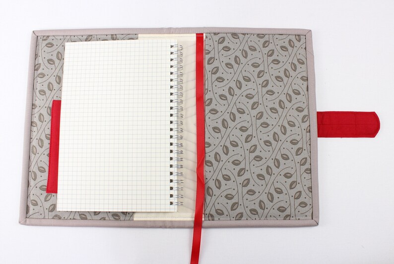 May include: A grey fabric notebook cover with a red ribbon bookmark and a red fabric closure. The cover features a pattern of brown leaves on a light grey background.