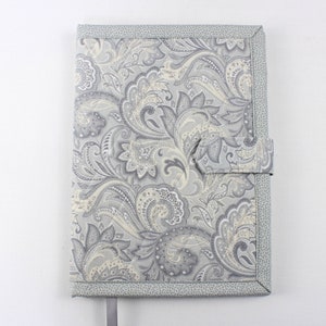 Pu&ograve; includere: Una copertina per libro in tessuto con motivo paisley grigio e bianco con un cinturino in tessuto grigio.