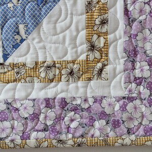 May include: Close-up of a quilt corner with a white background and a border of yellow and purple floral fabric. The quilt is quilted with a wavy pattern.