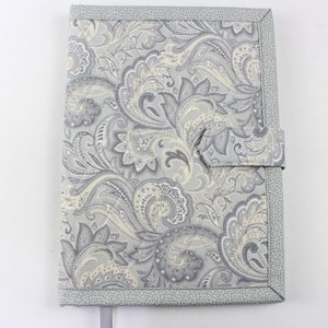 Pu&ograve; includere: Una copertina per libro in tessuto con motivo paisley grigio e bianco con chiusura a lembo in tessuto grigio e un segnalibro in nastro grigio.
