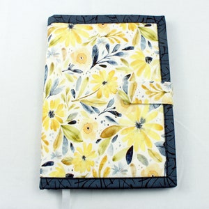 May include: A blue and yellow floral fabric book cover with a strap closure. The cover has a watercolor-style design with yellow flowers and blue leaves.