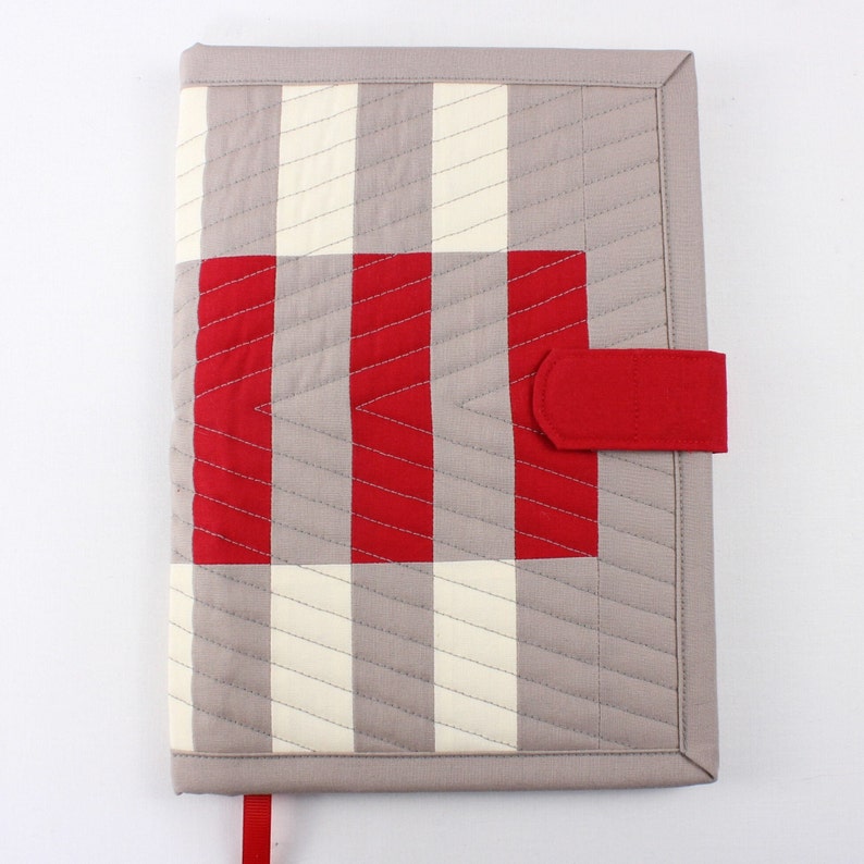 May include: A grey and white striped fabric book cover with a red flap closure. The cover has a red and white chevron pattern in the centre.