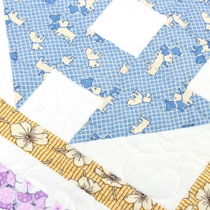 May include: A quilt with a patchwork design featuring a blue fabric with a white grid pattern and white dog silhouettes, a white fabric, and a yellow fabric with a white floral pattern.
