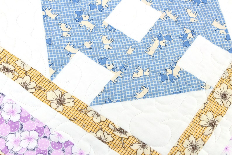 May include: A quilt with a patchwork design featuring a blue fabric with a white grid pattern and white dog silhouettes, a white fabric, and a yellow fabric with a white floral pattern.