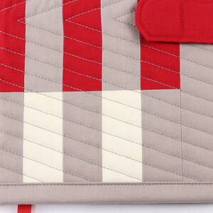 May include: A grey and red quilted fabric notebook cover with a red fabric closure strap. The cover has a chequered pattern with diagonal stitching.