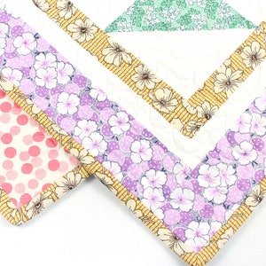May include: Close-up of a quilt with a patchwork design. The quilt features a variety of floral patterns in shades of pink, purple, and green, with a yellow border.