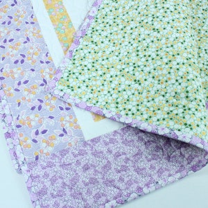 Puede incluir: Una colcha de retazos con un patr&oacute;n floral en tonos de morado, verde y amarillo. La colcha est&aacute; hecha de diferentes telas con varios dise&ntilde;os florales.