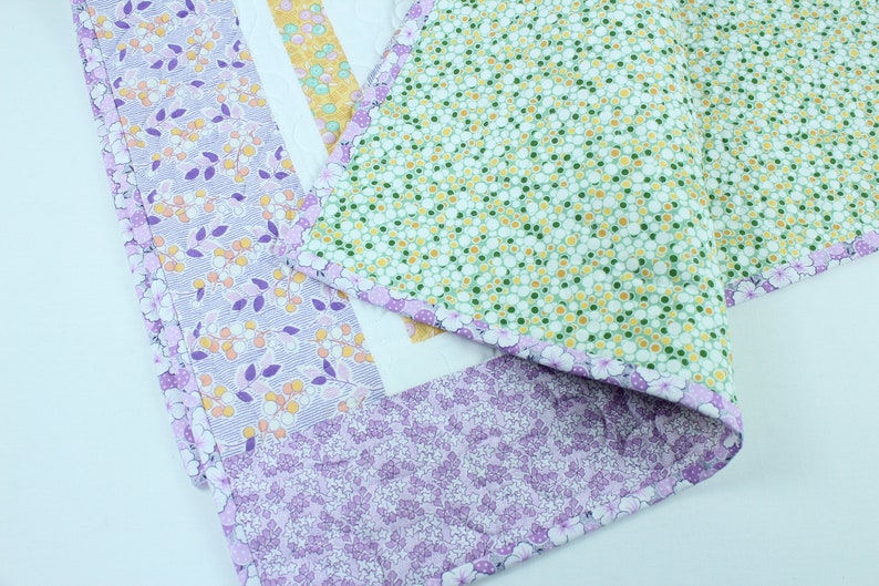 Puede incluir: Una colcha de retazos con un patr&oacute;n floral en tonos de morado, verde y amarillo. La colcha est&aacute; hecha de diferentes telas con varios dise&ntilde;os florales.
