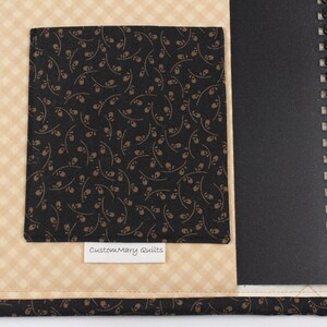 Puede incluir: Una cubierta de cuaderno de tela negra y marr&oacute;n con un bolsillo de tela negra y una etiqueta blanca que dice "CustomMary Quilts".