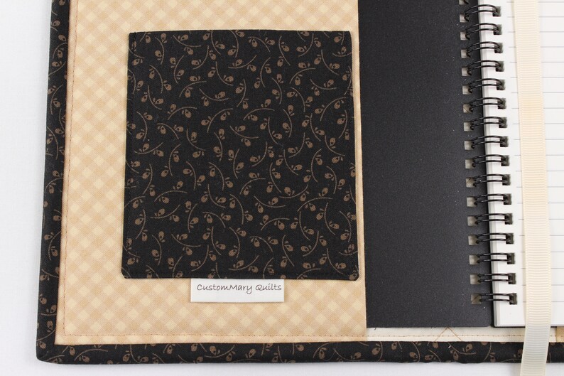 Puede incluir: Una cubierta de cuaderno de tela negra y marr&oacute;n con un bolsillo de tela negra y una etiqueta blanca que dice "CustomMary Quilts".