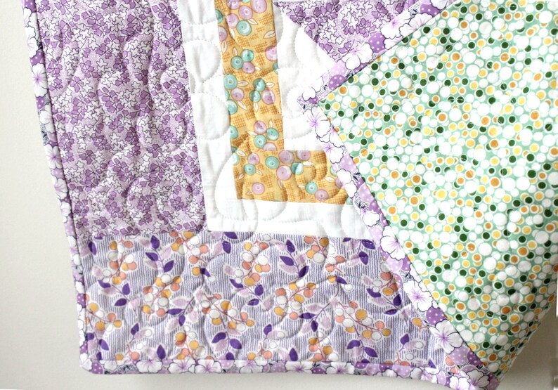 Puede incluir: Una colcha de retazos de color morado, verde y amarillo con un patr&oacute;n floral. La colcha est&aacute; hecha de diferentes telas y tiene un dise&ntilde;o acolchado.