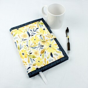 May include: A blue and yellow floral fabric journal cover with a white ribbon bookmark. The cover has a flap that closes with a snap.