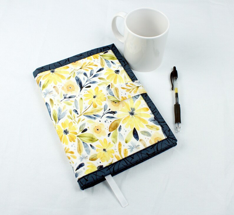 May include: A blue and yellow floral fabric journal cover with a white ribbon bookmark. The cover has a flap that closes with a snap.