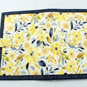 May include: A blue fabric book cover with a yellow floral pattern. The cover has a strap closure.
