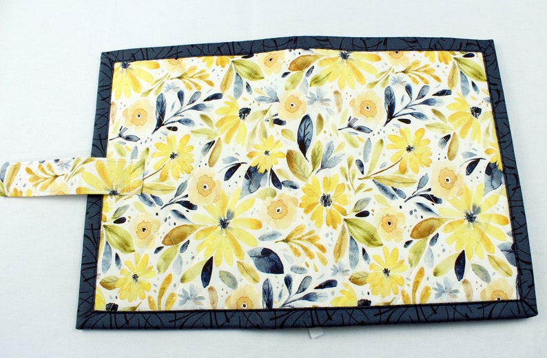 May include: A blue fabric book cover with a yellow floral pattern. The cover has a strap closure.