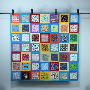 May include: A colorful quilt with a patchwork design featuring various patterns and colors. The quilt is made up of 36 squares, each with a different design. The quilt is hanging on a wall.