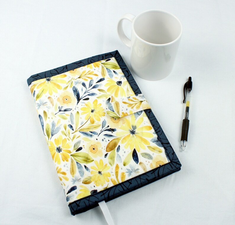 May include: A blue and white floral notebook cover with a yellow floral pattern. The cover has a flap that closes with a velcro closure.