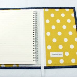 May include: A yellow and white polka dot fabric notebook cover with a blue floral fabric pocket and a white ribbon bookmark. The cover has a blue fabric border and the text "Custom Mary Quilts" is printed on the front.