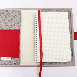May include: A grey fabric notebook cover with a red ribbon bookmark and a red fabric pocket. The cover has a leaf pattern and the text "Customizing Beauty" is printed on the pocket.