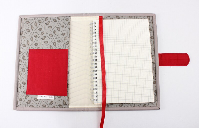 May include: A grey fabric notebook cover with a red ribbon bookmark and a red fabric pocket. The cover has a leaf pattern and the text "Customizing Beauty" is printed on the pocket.