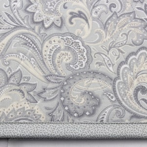Pu&ograve; includere: Un tessuto a fantasia paisley grigio e bianco con un bordo grigio. Il tessuto ha una texture trapuntata sottile.