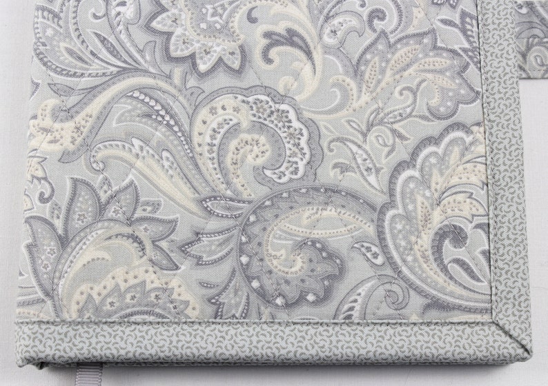Pu&ograve; includere: Un tessuto a fantasia paisley grigio e bianco con un bordo grigio. Il tessuto ha una texture trapuntata sottile.