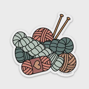 May include: A sticker featuring a collection of yarn balls in shades of peach, teal, and gray, with two wooden knitting needles. The sticker has a white border and includes the text "CAMP STITCHWOOD".