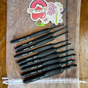 May include: A set of ten black crochet hooks in a white mesh bag. The hooks are labeled with their size and corresponding measurement in millimeters. The sizes are 10/0, 9/0, 8/0, 7.5/0, 7/0, 6/0, 5/0, 4/0, 3/0, and 2/0.