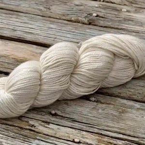 May include: A skein of off-white yarn, wound into a loose coil, on a rustic wooden surface.