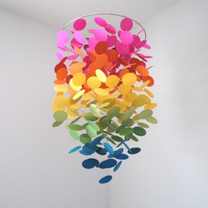 May include: A rainbow-colored mobile made of paper circles hanging from a metal ring. The circles are arranged in a gradient from pink to red, orange, yellow, green, blue, and purple.