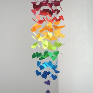 Puede incluir: Un móvil de colores arcoíris hecho de corazones de papel que cuelgan de un anillo de metal. Los corazones están dispuestos en un degradado de rojo a morado.