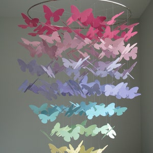 May include: A rainbow-colored mobile made of paper butterflies. The butterflies are arranged in a cascading pattern, with the pink butterflies at the top and the yellow butterflies at the bottom.