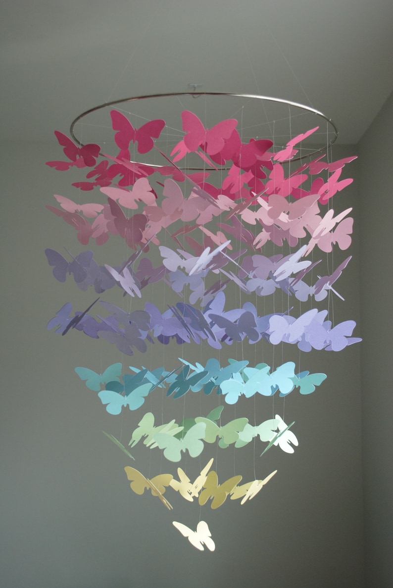 May include: A rainbow-colored mobile made of paper butterflies. The butterflies are arranged in a cascading pattern, with the pink butterflies at the top and the yellow butterflies at the bottom.