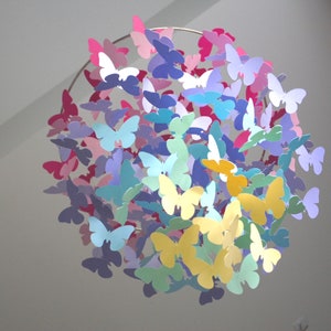 May include: A colorful paper butterfly mobile with butterflies in shades of pink, purple, blue, yellow, and green hanging from a circular metal frame.